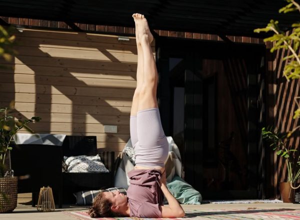 A woman performing a shoulder stand yoga pose on a sunny outdoor patio, enhancing flexibility and mindfulness.